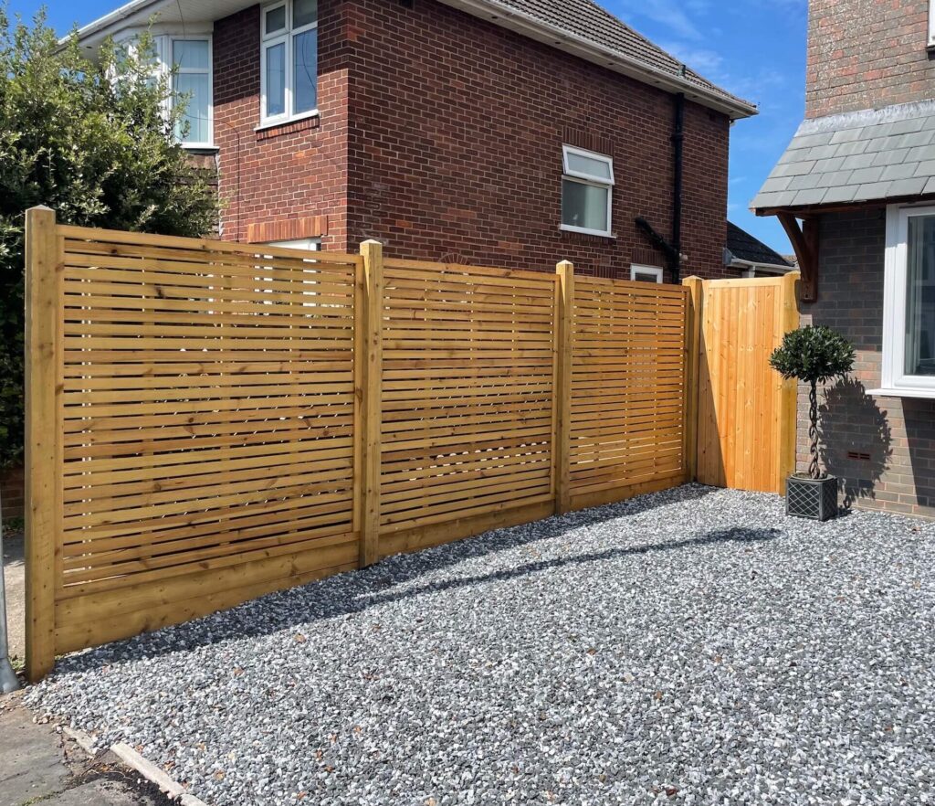 Horizontal slatted fence and matching gate beside a gravel driveway