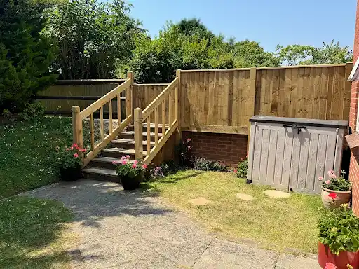Timber garden steps with handrails up to a fenced lawn